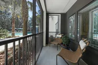 Sunny balcony with wicker chairs overlooking a lush pool area.