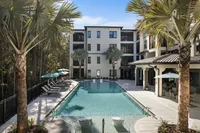 Modern apartment complex with a luxurious swimming pool surrounded by palm trees and sun loungers.