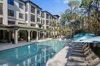 Modern apartment complex with a pristine swimming pool surrounded by lush greenery and sun loungers.