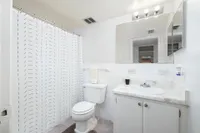 Bright bathroom featuring a modern white vanity, textured shower curtain, and large mirror.