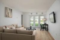 Bright living room with beige sofa, wall-mounted TV, and patio doors leading to garden.