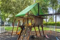 Charming outdoor playground with climbing wall, swings, slide, and wooden playhouse surrounded by lush greenery.