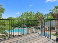Charming apartment balcony view overlooking a luxurious pool surrounded by lush greenery and palm trees.