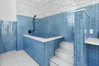 Chic bathroom with vibrant blue tiles, unique cartoon-themed wall design, and elegant built-in steps leading to a luxurious tub.