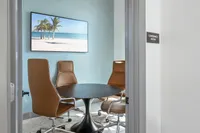Inviting conference room with a round table, stylish leather chairs, and tropical beach artwork creating a serene ambiance.