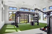 Bright and modern fitness room with state-of-the-art equipment, featuring TRX system, kettlebells, and vibrant greenery outside large windows.
