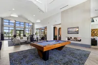 Luxurious apartment lounge with high ceilings, modern decor, pool table, and large windows offering natural light.