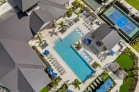 Aerial view of a luxurious apartment complex featuring a stunning swimming pool, lush landscaping, and recreational tennis courts.