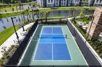 Luxurious apartment complex featuring a pristine tennis court surrounded by lush greenery and serene water views, perfect for active living.