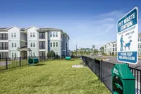 Modern apartment building with pet-friendly amenities, fenced green area, and convenient pet waste station, perfect for pet owners.