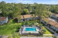 Charming apartment complex surrounded by lush greenery, featuring a central outdoor pool and sun deck area.