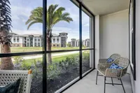 Inviting screened balcony with cozy wicker chairs overlooking lush palm trees and modern apartment buildings.