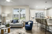 Chic living room with modern furniture, elegant rug, and open kitchen featuring bar seating and ample natural light.