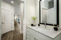 Bright and modern bathroom with elegant vanity, framed mirror, and sleek wood flooring leading to a cozy living space.
