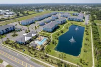 Scenic aerial view of a luxury apartment complex with modern buildings, a sparkling swimming pool, and a serene pond with fountains.