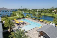 Luxury apartment complex with beautiful palm-lined pool area, vibrant yellow umbrellas, and scenic lake view, offering resort-style living.