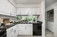 Contemporary kitchen with sleek white cabinets and black countertops, leading into a bright living area with lush garden views.