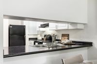 Modern kitchen with sleek black countertops, stainless steel sink, and stylish appliances creating a welcoming culinary space.