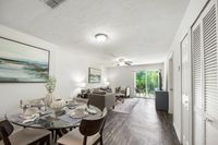Bright and elegant apartment interior with open-plan living and dining area, featuring modern furniture, a stylish glass dining table, and a view of the lush green garden through large sliding doors.