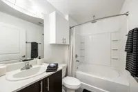 Modern, bright bathroom featuring a sleek countertop sink, elegant cabinetry, and a spacious white bathtub with a curved shower rod.