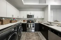 Modern kitchen with sleek black and white cabinetry, stainless steel appliances, and a convenient laundry area, creating a stylish and functional space.