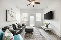 Chic and airy living room with modern decor, large leather sofa, wall-mounted TV, and elegant ceiling fan, perfect for relaxation.