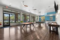 Inviting recreation room with modern design featuring table tennis, shuffleboard, and vibrant seating, overlooking lush greenery and a swimming pool.