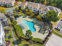 Lush apartment complex featuring a resort-style pool, surrounded by palm trees, sun loungers, and a covered patio area for relaxation.