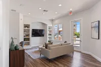 Bright and modern living room with elegant decor, featuring a stylish leather sofa, built-in shelves, and a large flat-screen TV, all set against a backdrop of sleek hardwood flooring and abundant natural light from large windows.