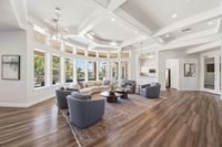 Elegant living room with floor-to-ceiling windows, modern chandelier, cozy seating area, and rich wooden flooring, offering abundant natural light and a welcoming atmosphere.
