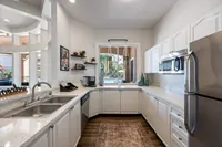 Bright and modern kitchen with sleek white cabinets, stainless steel appliances, and a window view of lush greenery, perfect for culinary inspiration.