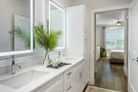 Modern bathroom with elegant double vanity, illuminated mirrors, and a view into a cozy bedroom, accentuated by natural light through large windows.