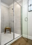 Elegant glass shower enclosure with sleek gray tiles, complemented by a wooden stool for added luxury.
