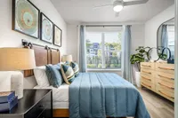Inviting bedroom with stylish decor featuring a comfortable blue bedding set, elegant artwork, and abundant natural light from large windows overlooking lush greenery.