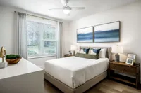 Bright and cozy bedroom with modern decor, featuring large windows, elegant artwork, and stylish wooden furniture.