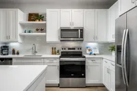 Modern kitchen with sleek white cabinetry, stainless steel appliances, and elegant open shelving.