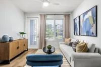 Elegant living room with modern decor, featuring a plush white sofa, vibrant abstract art, and a stylish console table beneath a bright window.