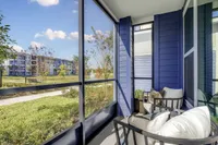 Charming screened balcony with plush seating, overlooking lush greenery and a picturesque pond. Modern blue siding adds a touch of elegance.