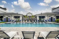 Luxurious apartment complex featuring a stunning outdoor pool surrounded by elegant lounge chairs and modern architecture under a bright blue sky.