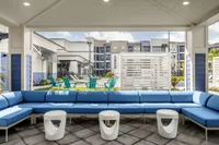 Inviting outdoor lounge area with chic blue seating and modern white tables, overlooking a vibrant community space and pool.