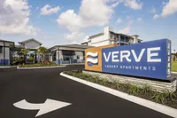 Inviting entrance of Verve Luxury Apartments with modern architecture and lush landscaping under a picturesque sky.