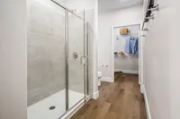 Modern bathroom with elegant glass shower and walk-in closet, featuring stylish wooden flooring and ample natural light.