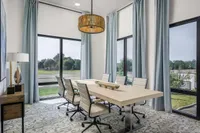 Elegant dining room with large windows, modern wooden table, and soft blue curtains offering a serene view of greenery.