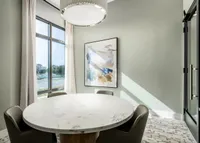 Elegant dining corner with a round marble table, modern artwork, and large windows flooding the area with natural light.
