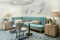 Chic lounge area with a teal tufted bench, stylish marble tables, and comfy modern chairs, accentuated by artistic wall decor and soft ambient lighting.