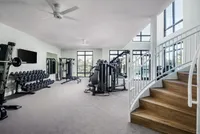 Modern fitness center with state-of-the-art equipment, free weights, and bright natural lighting, featuring sleek design and inviting staircase.