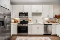 Elegant modern kitchen with white cabinets, stainless steel appliances, and stylish backsplash.