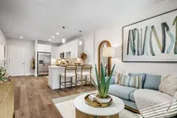 Contemporary open-concept living room with chic decor, cozy sofa, stylish artwork, and modern kitchen featuring sleek appliances and bar seating.