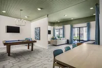Modern and inviting apartment interior showcasing a chic game room with a pool table, elegant sitting area, and large windows offering plenty of natural light.