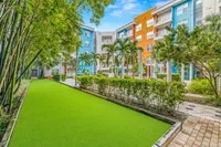 Vibrant apartment complex with colorful facades, lush greenery, and a well-maintained walkway under a clear blue sky.